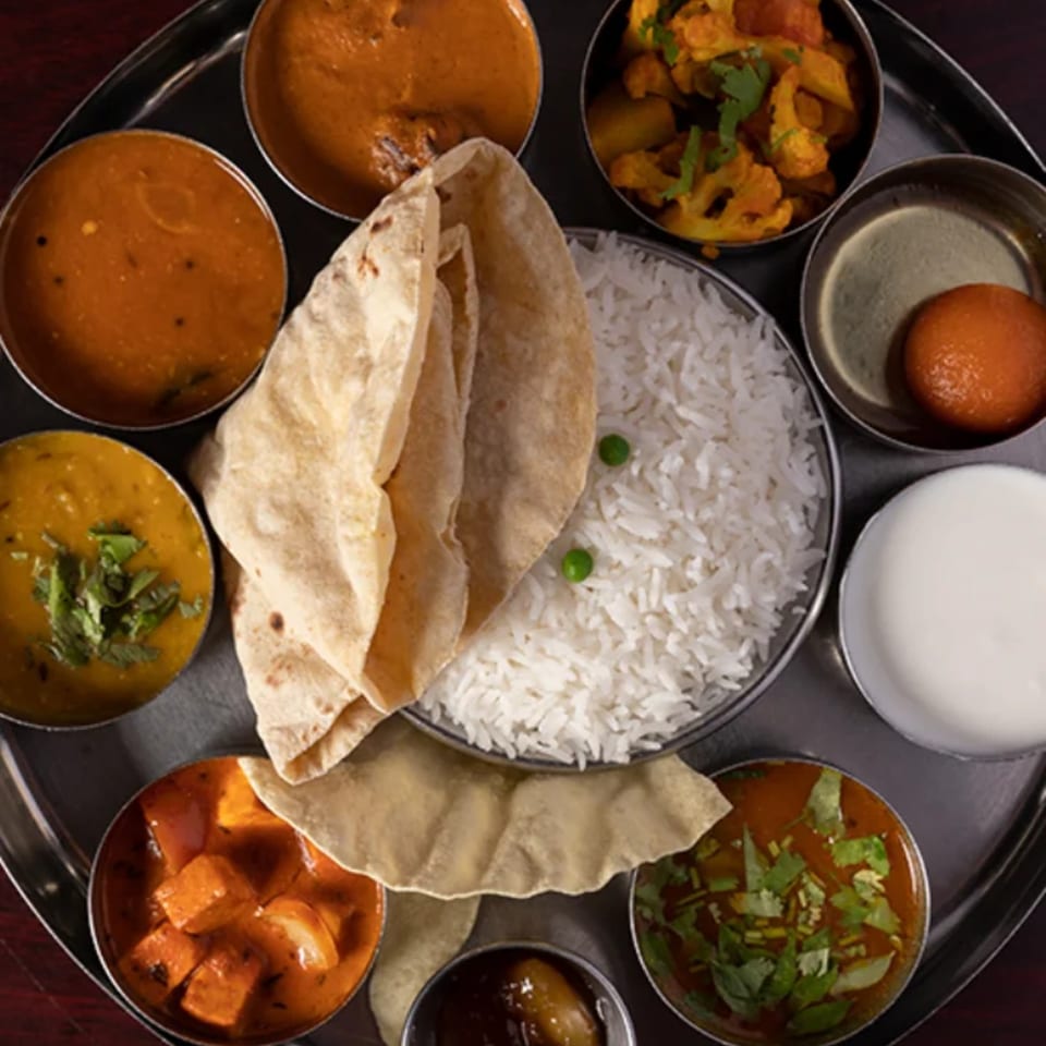 A Udupi Cafe thali with various Indian dishes, including rice, curries, bread, and dessert.