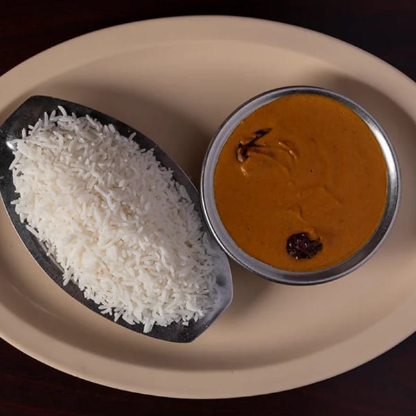 A serving of white rice in a metal dish next to a bowl of orange curry on a beige plate.