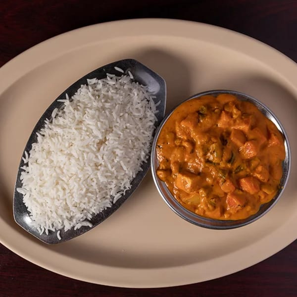 Indian butter chicken or paneer curry with white rice on a beige plate at Udupi Cafe.