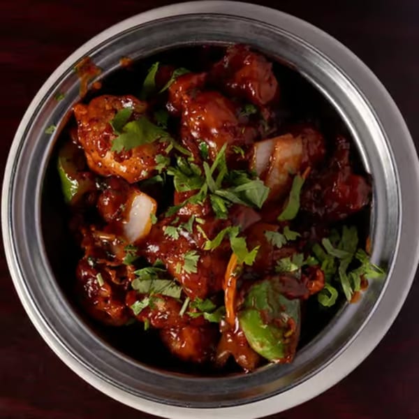 A close-up of Udupi Cafe's Gobi Manchurian, featuring crispy cauliflower in a rich, dark sauce with cilantro.